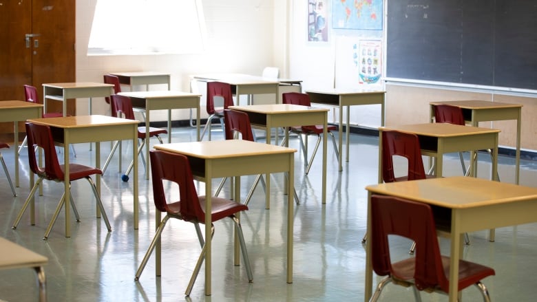 Empty desks and chairs are spaced out in a bright classroom.