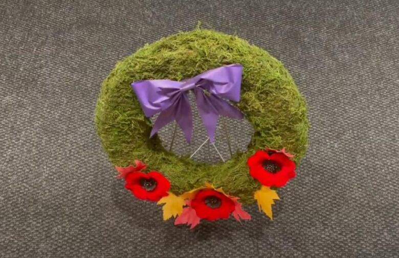 A green wreath featuring poppies and a purple bow.