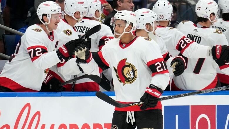 A hockey player gets high-fives from teammates as he skates by the bench.