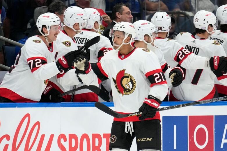 A hockey player gets high-fives from teammates as he skates by the bench.