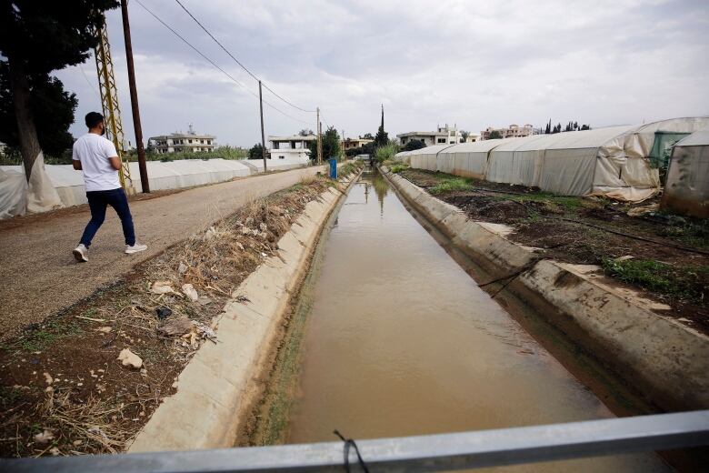 A man walks beside a murky canal