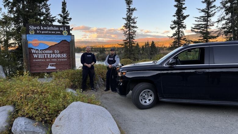 Two men standing beside a black SUV.