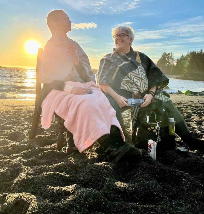 Two women sit side-by-side on a beach.