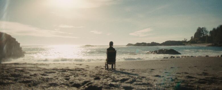 A woman sits on a beach with her back to camera. She is backlit.