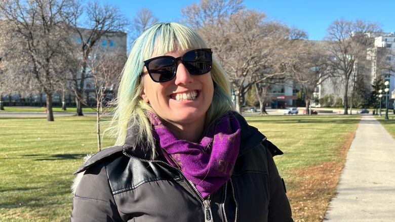 A woman with blue and blonde hair, wearing sunglasses, is smiling at the camera.