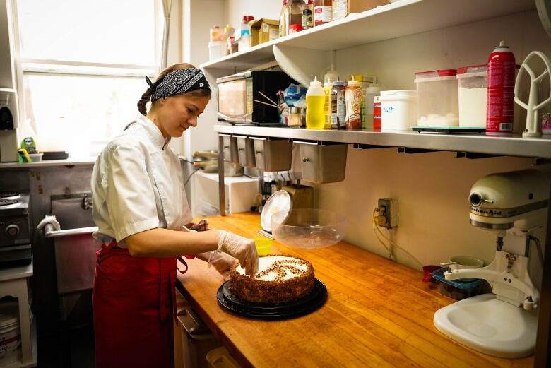 A woman decorates a cake in large kitchen.