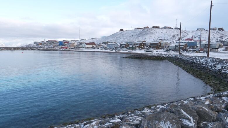 Water, shoreline, buildings sprinkled with snow. 