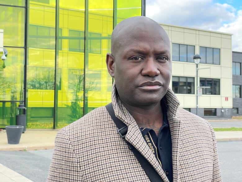 Portrait of man with a serious expression outside a building of greenish glass.