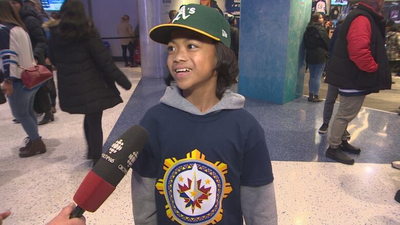 A young Filipino boy in a Winnipeg Jets jersey with a new Filipino-inspired logo smiles as he talks to a reporter inside the team's arena.