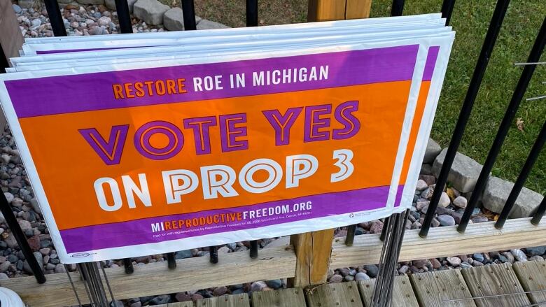 A stack of orange and purple lawn signs that read 'Restore Roe in Michigan: Vote Yes on Proposal 3' 