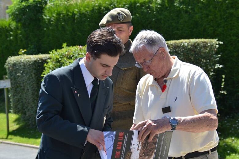 Two men look down at a book they are both holding.