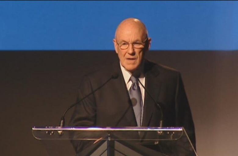 Bald man with glasses standing at a lectern.