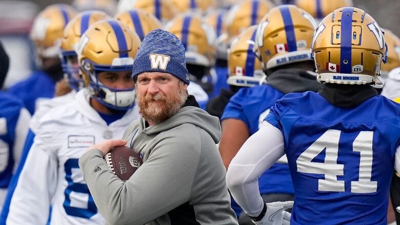 Surrounded by his players, Winnipeg Blue Bombers head coach Mike O'Shea walks with the football during practice ahead of the 108th CFL Grey Cup against the Hamilton Tiger-Cats in Hamilton, Ont., on Wednesday, Dec. 8, 2021.