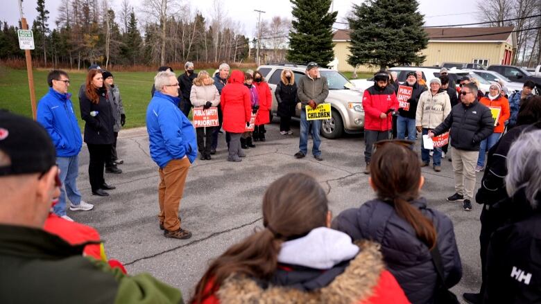 A group of people stand in a circle in a parking lot while holding signs that say 'protect our children' and 'public safety is a priority.'