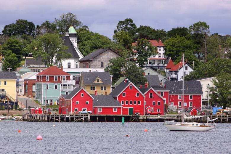 Red wooden buildings are shown on the shore in a photo of the Lunenburg waterfront.