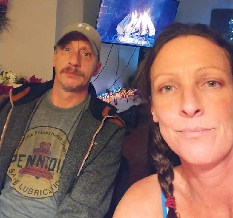 A man and a woman take a selfie with the Christmas fire log playing on a screen behind them.