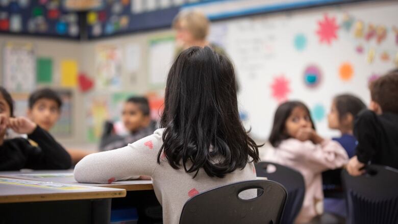 A student sits in a classroom with their face away from the camera.