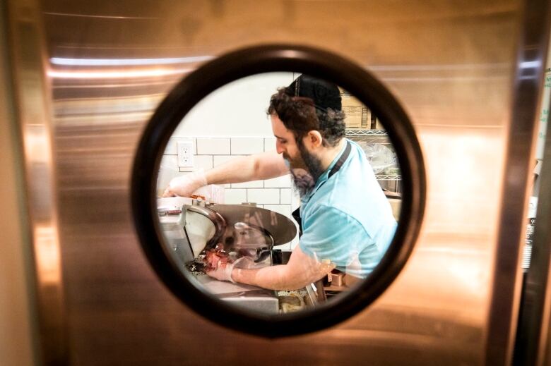 A man with a brimless cap works in a kitchen.