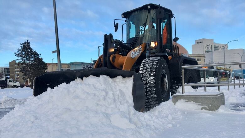 A front-end loader pushes a large mound of snow on a city street.