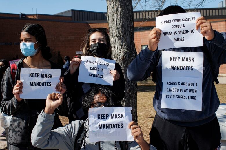 A group of high school-aged students wearing masks hold up signs that say 