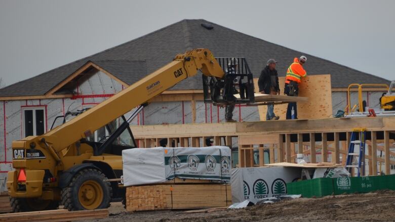 Construction workers stand on partly built house in the Hanmer area of Greater Sudbury, surrounded by machines, piles of lumber and other houses under construction.