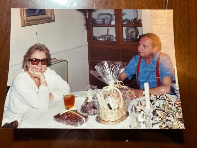 A man and a woman sit together at a dining table. The man looks at the woman as she smiles for the camera.