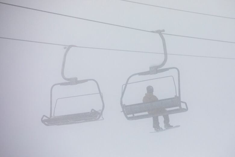 A snowboarder sits on a ski lift in hazy conditions.