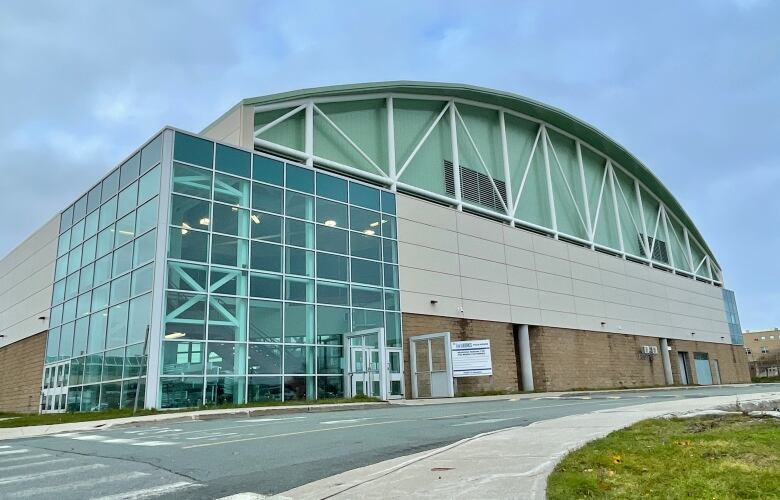 A large building stands with an arched roof and a glass extension on the left corner.