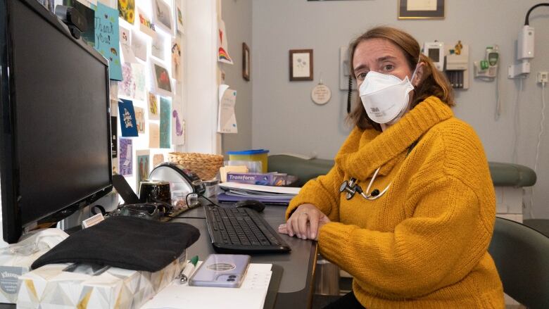 Dr. Nili Kaplan-Myrth wears a mask as she sits at a desk and computer.