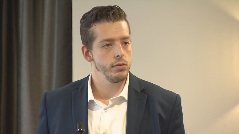 Man looking slightly off camera wearing white shirt and navy blazer.