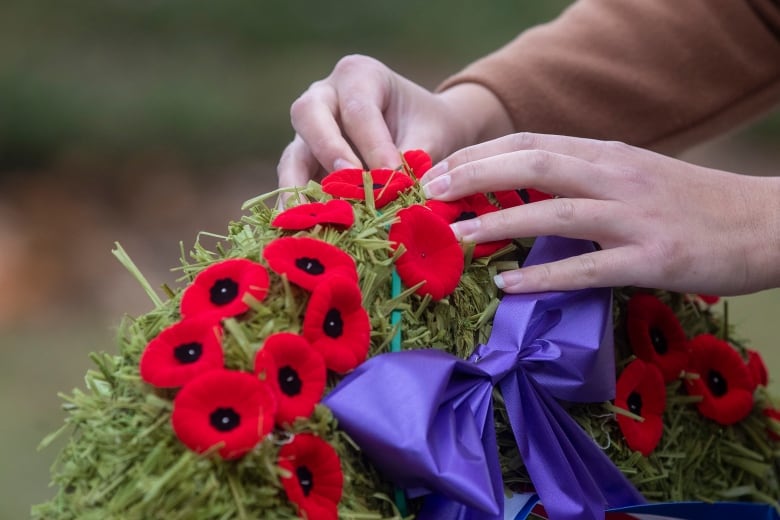 Someone attaches a poppy to a commeorative wreath.