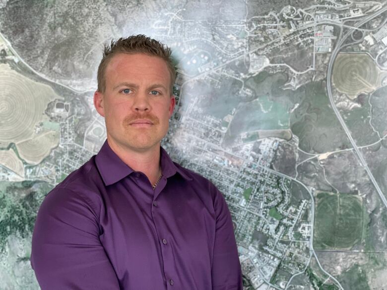 A man in a purple button up stands in front of a wall map.