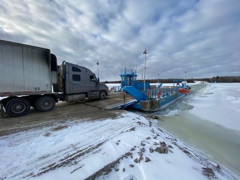 A semi sits waiting to board the ferry across the snowy Nelson River.