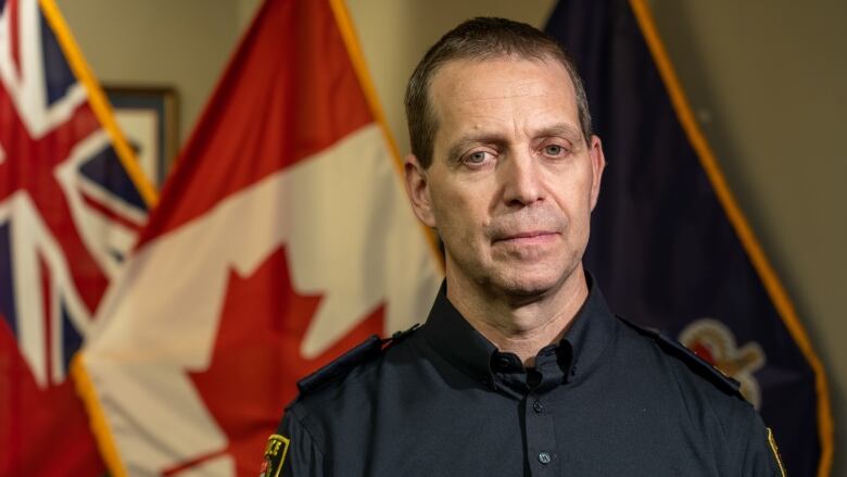 A police officer poses for a photo with flags behind him.