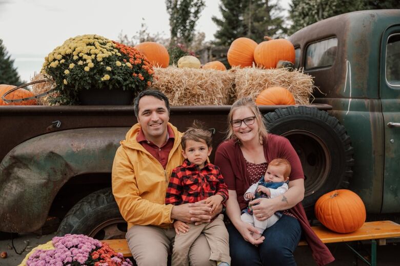 A man and a woman sit on a bench with their two young kids in a pumpkin patch.