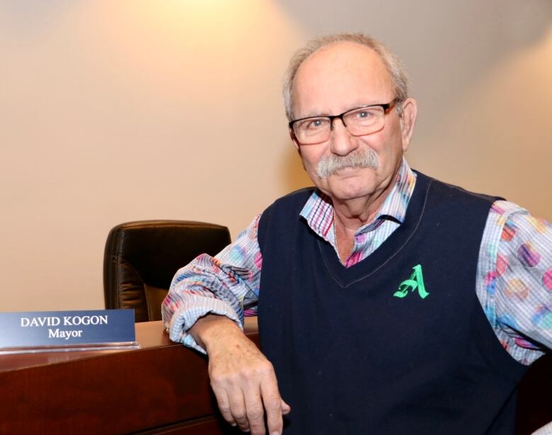 A man with grey hair who's wearing a sweater vest and glasses poses for a photo.