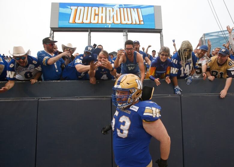 Fans in the stands cheer in front of a large screen reading 