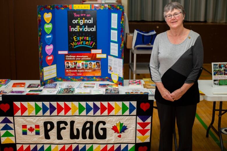 An older woman stands in front of a colourful LGBTQ booth.