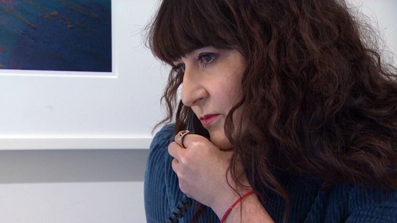 A close-up photo shows the profile of a white woman with long, curly dark hair holding a telephone handset to her ear.