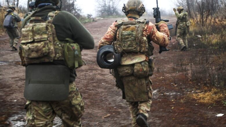 Four individuals in camoflage running in the opposite direction from the camera.