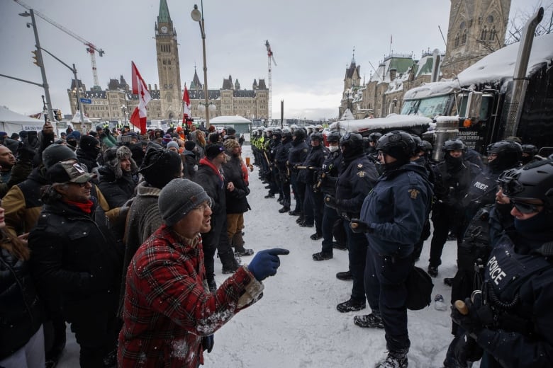 Protesters and police standing face to face in Ottawa, with the parliament building in the background.