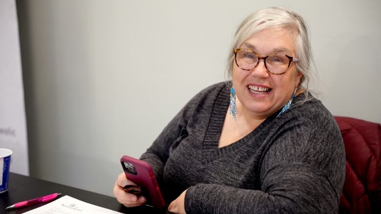 A woman with glasses and a grey sweater smiles into the camera. 