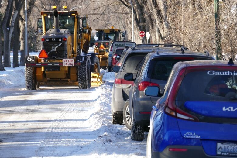 An orange grader travels up a Winnipeg residential street clearing snow.