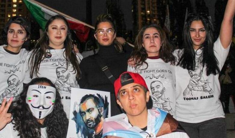 Young people wear shirts showing the image of the rapper Toomaj and hold signs. They are standing outside at a protest.