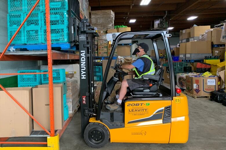 Man sits in forklift facing large shelving units where food has been stored.