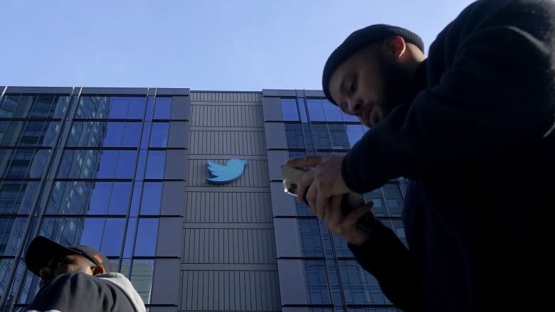 Two men walk past an office building with the Twitter logo on it.