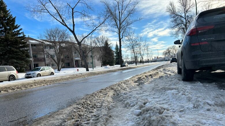 A car is parked on a street with snow piled up around it.