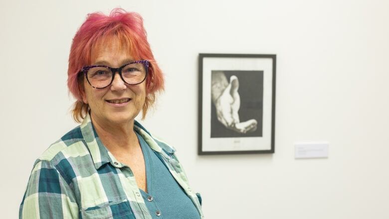 A woman in plaid stands in front of a sketch drawing of a hand reaching out.