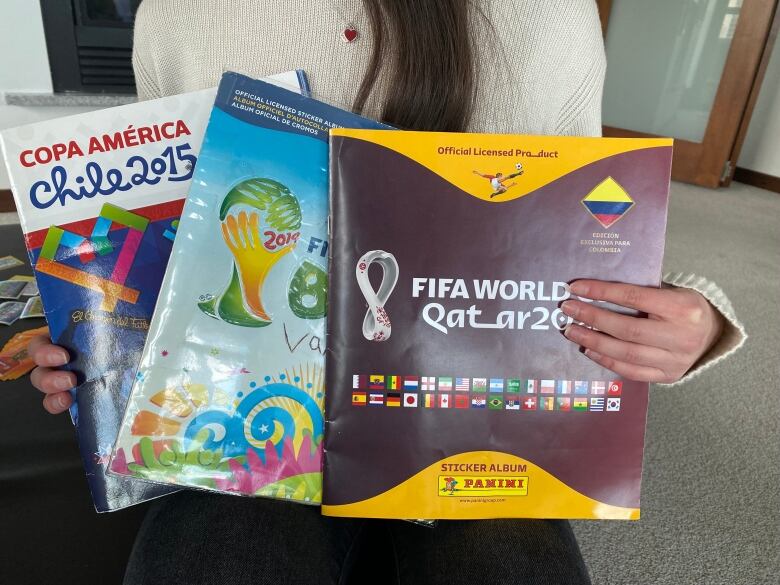 A woman holds up three paper sticker albums.