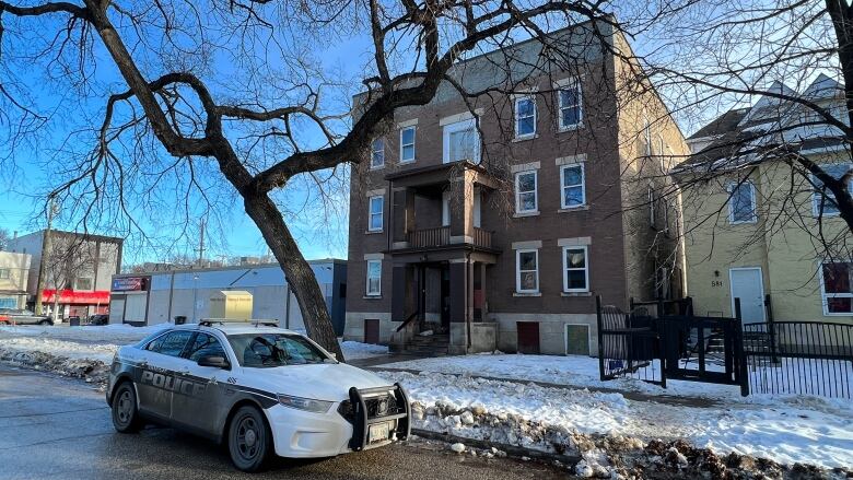 A police car is parked in front of an apartment building. There is snow on the ground.